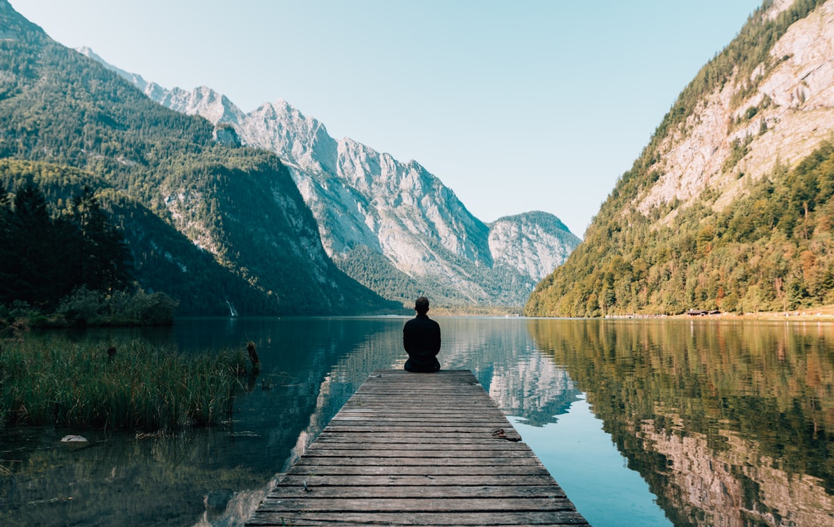 Traveller sitting on a jetty over a still alpine lake
