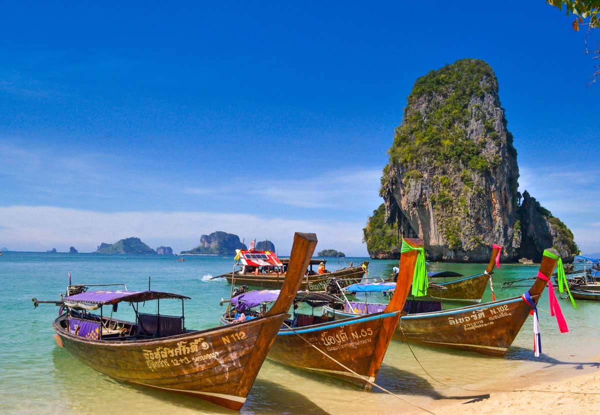 Longtail boats on a Thai beach beneath limestone cliffs